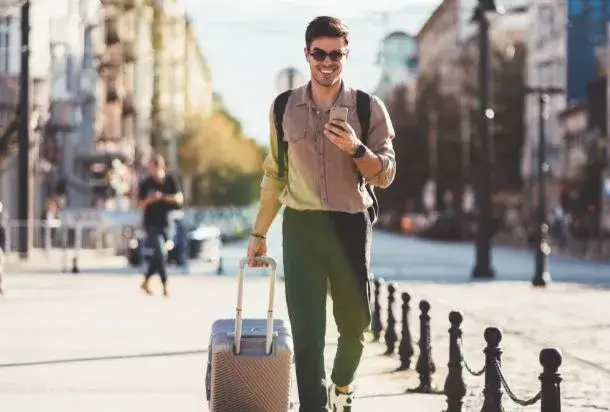 Man with a suitcase smiling at his phone